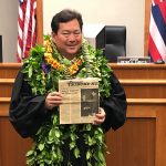 Third Circuit Court Judge Peter K. Kubota stands in front of his courtroom bench holding a copy of the 04/17/1974 edition of the Hawaii Tribune-Herald newspaper.